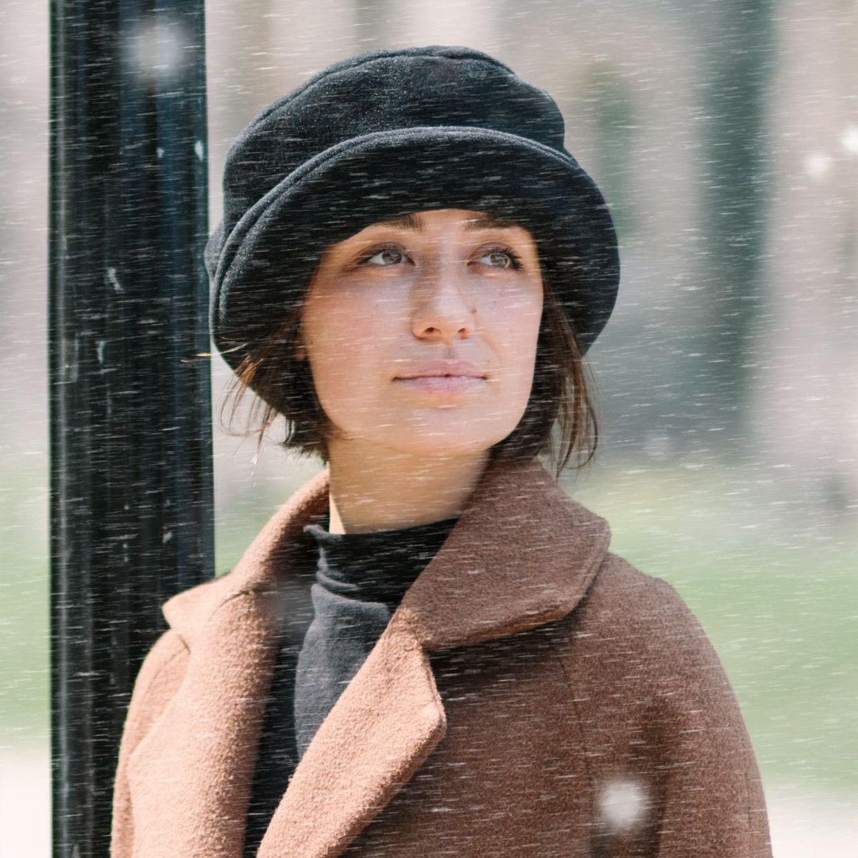 Woman in Black Fleece Rolled Brim Hat with Brown Wool Coat in gently falling snow