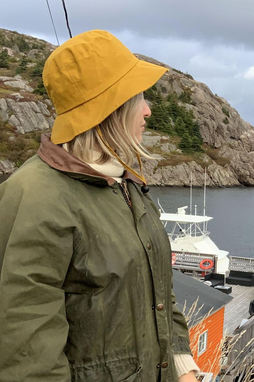 Woman wearing a Puffin Gear oilskin hat and rain coat looking over harbour in Quidi Vidi, Newfoundland, Canada