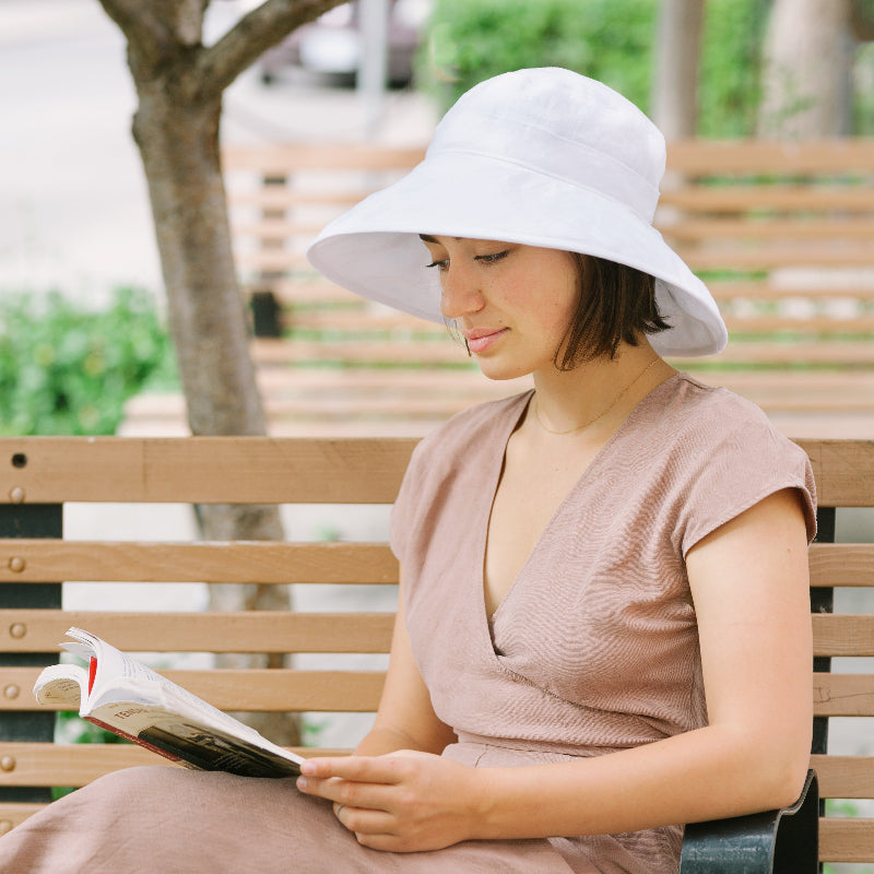 Wide Brim White Line Sun Hat on woman reading book on park bench-upf50 sun protection by puffin gear-made in canada