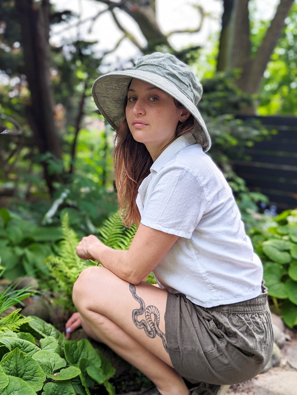 Women working in garden wearing wide brim linen UPF50 sun hat. Wild ginger , Japanese forest grass and ferns in garden