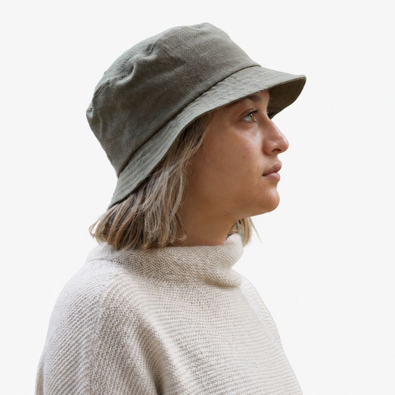 Woman Wearing olive green linen bucket hat and an ivory sweater on white background