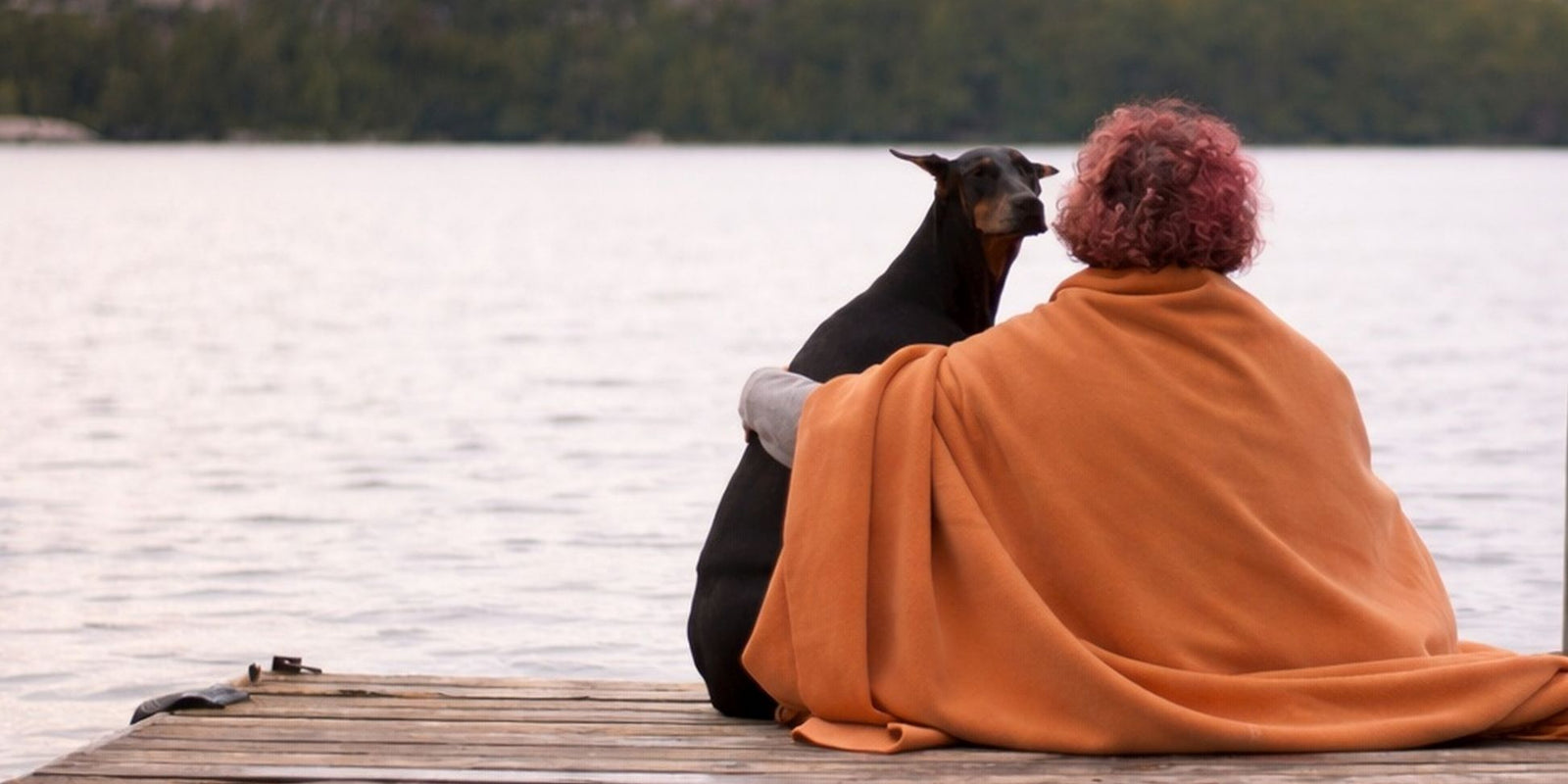 polartec 300 fleece blanket-pumpkin orange-woman wrapped in blanket sitting with dog on dock. made in canada-warm, durable, lightweight, best blanket you'll ever own